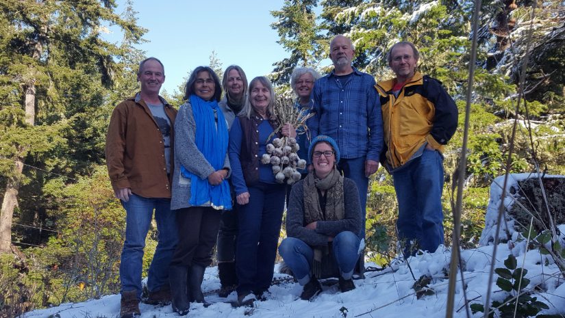 Transition land trust - Lohbrunner Community Farm Coop members and Heather Pritchard are gathered on a snow bank with a forest in the background. Heather is holding a bunch of garlic.