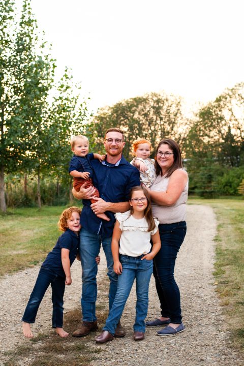 Suzanne and Mat Bergeron and their four children smiling outside surrounded by trees.