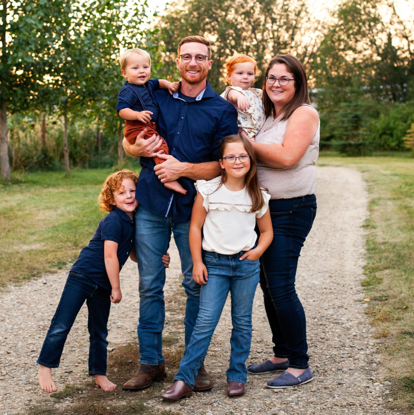 Suzanne and Mat Bergeron and their four children smiling outside surrounded by trees.
