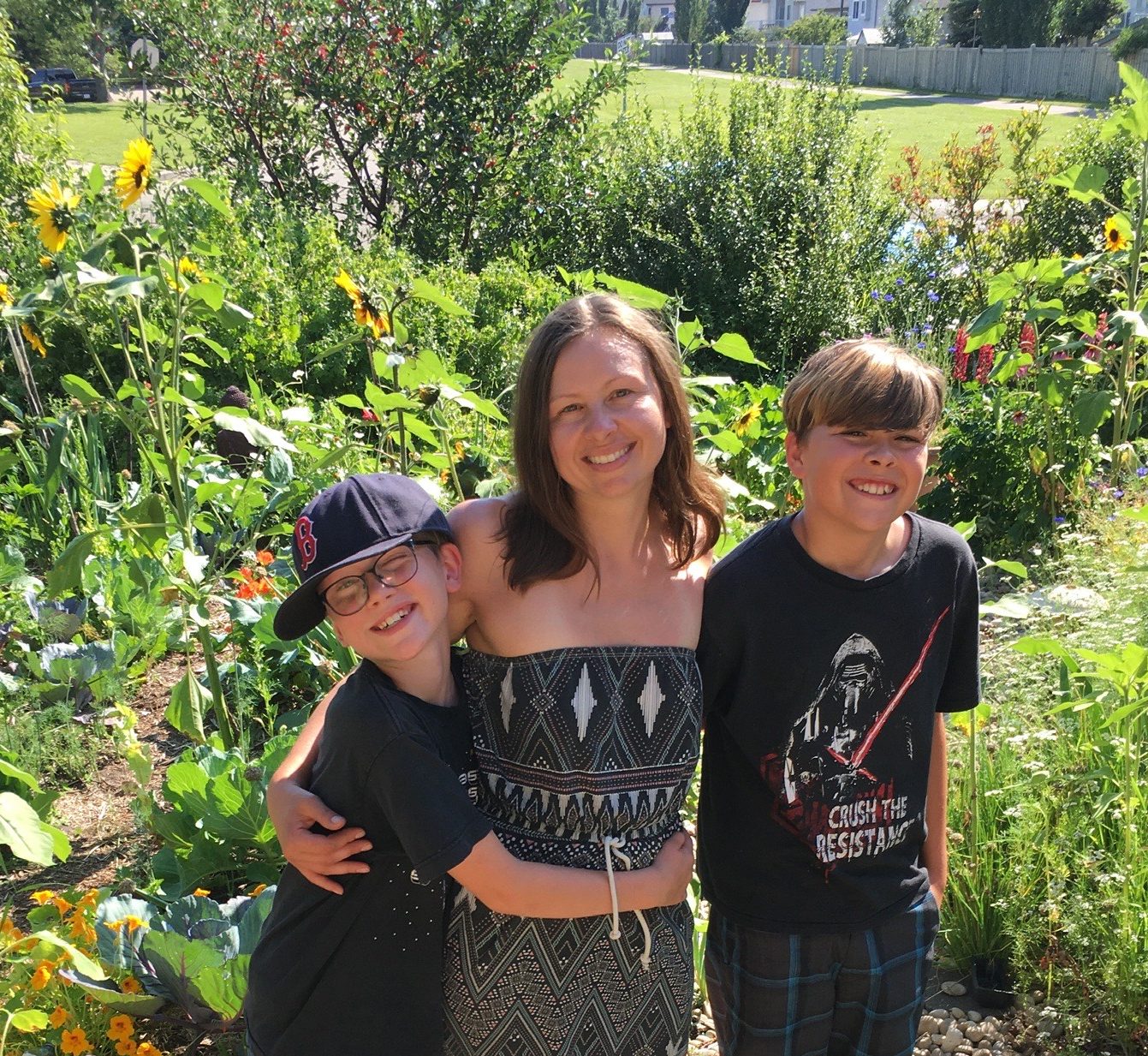Terra Pombert of Sunflowers Urban Farm smiles at the camera with her two young boys in her permaculture garden