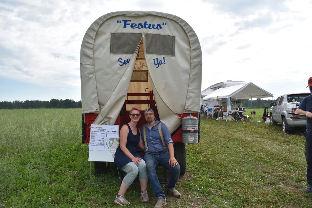 Anton Goulko and Dorothy Penner sitting on the fender of their farm stay covered wagon