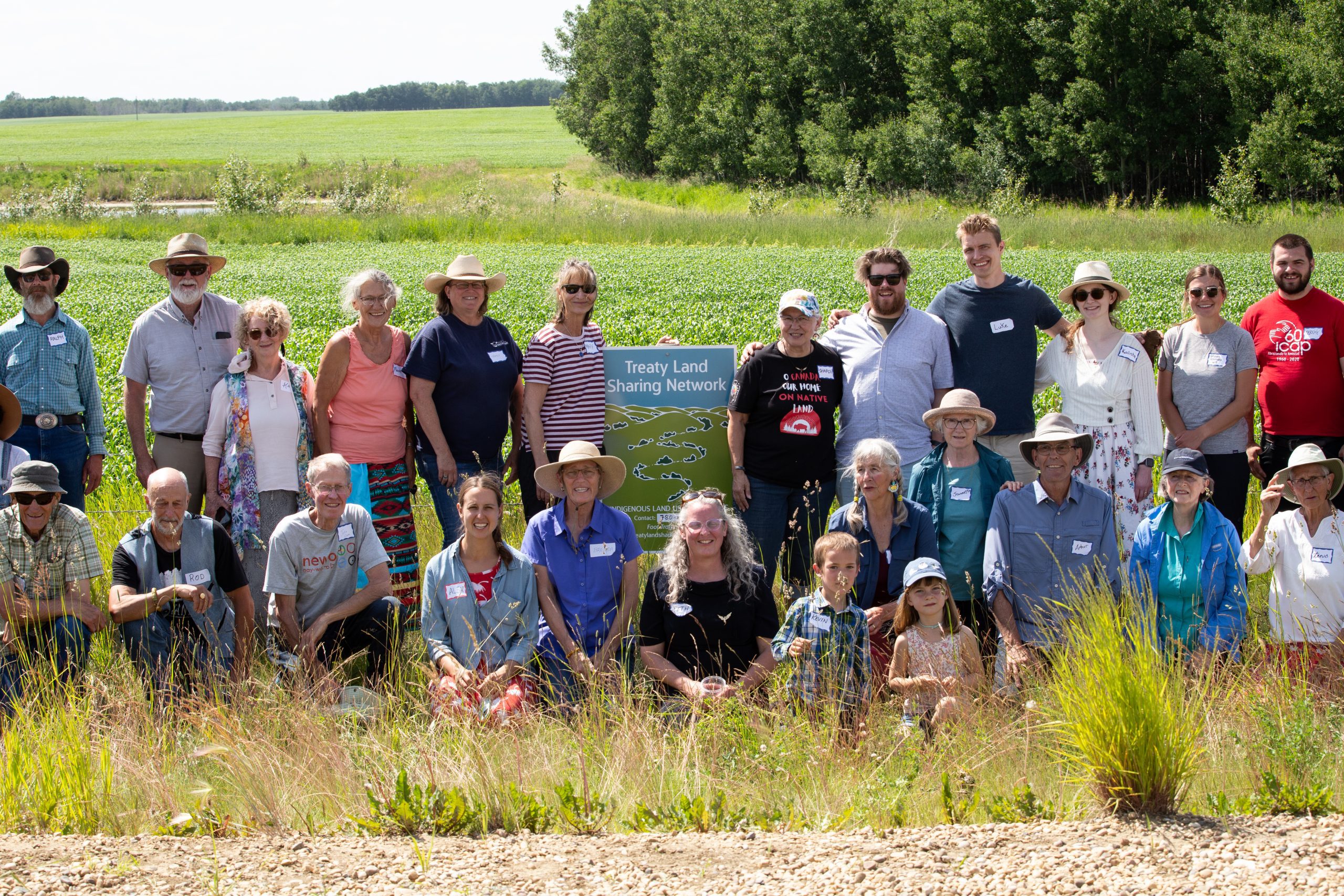 A group of people posing in front of the Treaty Land Sharing Network sign in a field